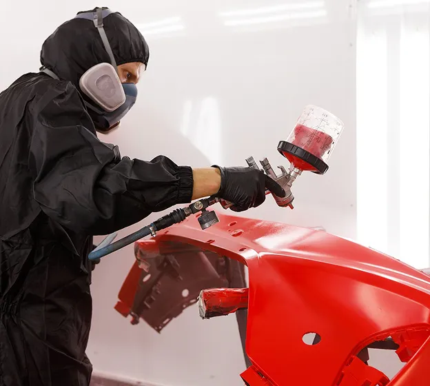 Carrossier peintre appliquant de la peinture rouge sur un élément de carrosserie